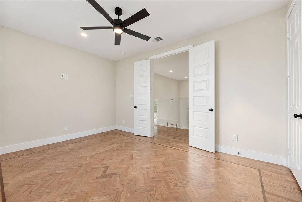 Herringbone wood-finish flooring, double panel doors, matte black ceiling fan with integrated light, and recessed lighting