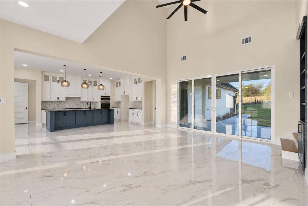 Vaulted ceilings, large-format tile flooring, oversized sliding glass doors, center kitchen island with dark cabinetry, and three pendant lights