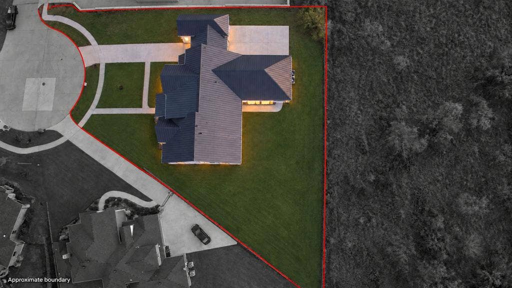 Aerial perspective of a property featuring a multi-gabled roofline, concrete driveway, sidewalk access, and a manicured lawn