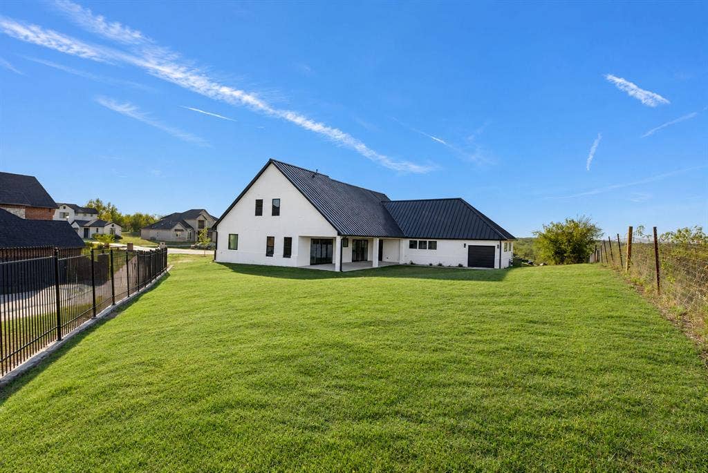 Exterior view featuring white siding, a black metal roof, a covered patio, an attached garage, and a fenced yard