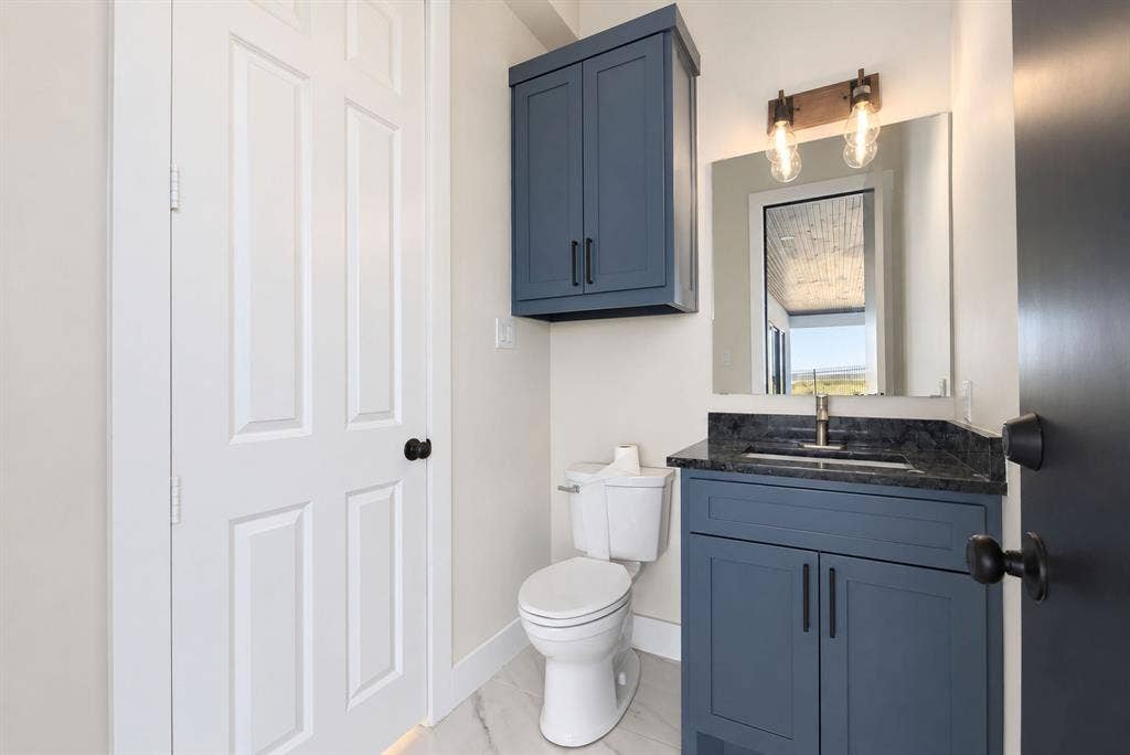 Custom navy-blue vanity and matching wall-mounted cabinet, dark stone countertop with an integrated rectangular sink, and industrial-style two-light wall fixture