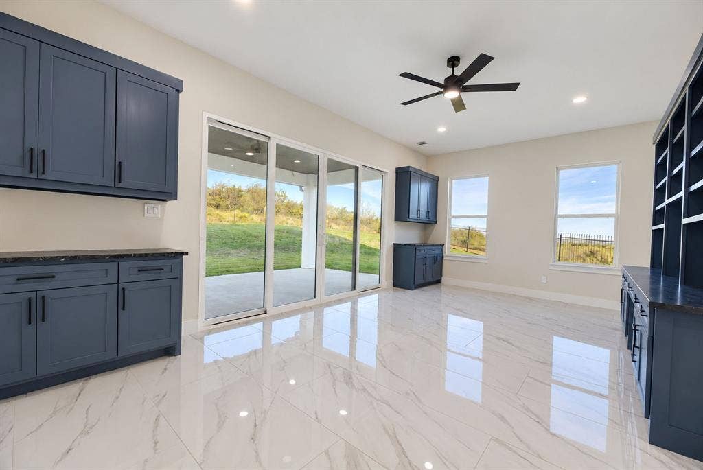 Large-format polished tile flooring, custom navy blue built-in cabinetry, floor-to-ceiling glass sliding doors, recessed lighting, and a modern ceiling fan