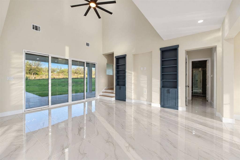 Vaulted ceilings featuring a multi-blade ceiling fan, expansive sliding glass doors, polished stone-finish tile flooring, and custom built-in floor-to-ceiling cabinetry