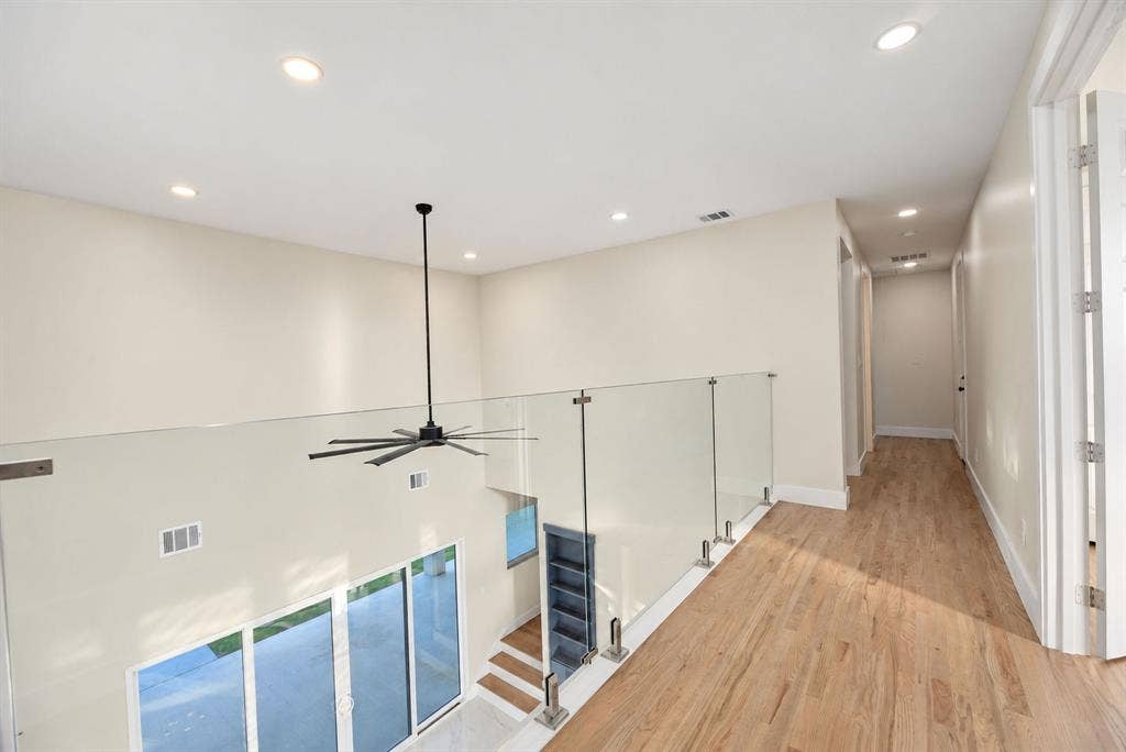 Upper hallway featuring wood-finish flooring, frameless glass panel railing with stainless steel hardware, and recessed ceiling lighting