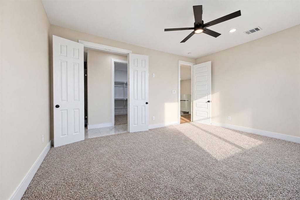 Neutral-toned interior featuring plush carpeting, a modern matte-black ceiling fan, multi-panel doors, and built-in closet shelving