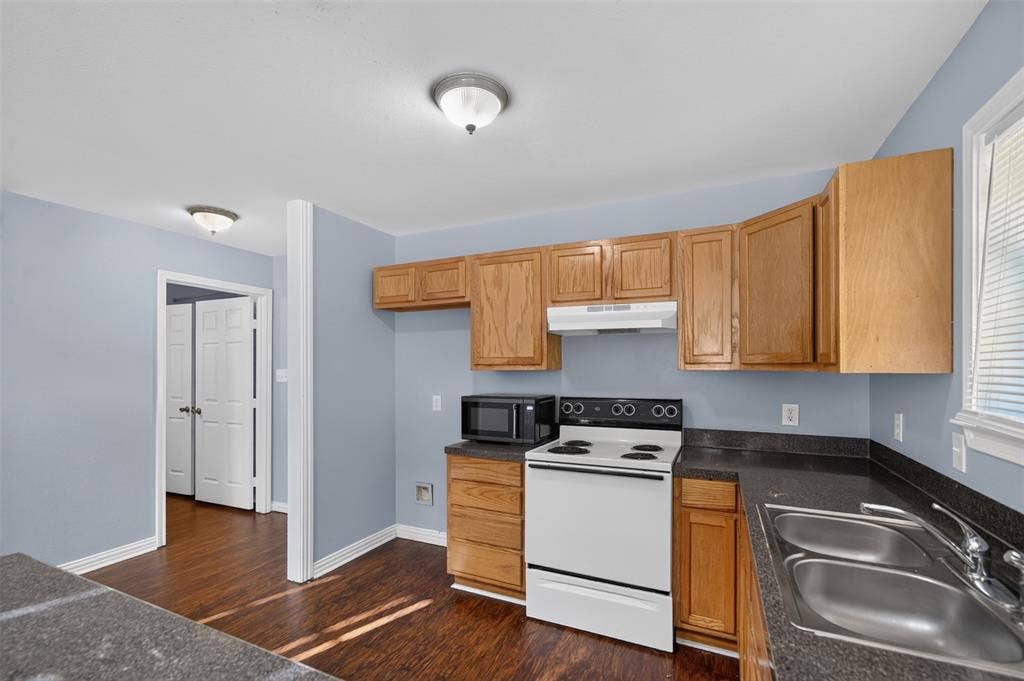 1708 Timber View Drive, Tyler, TX 75703 Kitchen featuring oak-finish cabinetry, dark solid-surface countertops, dual-basin stainless steel sink, electric range, and wood-finish flooring
