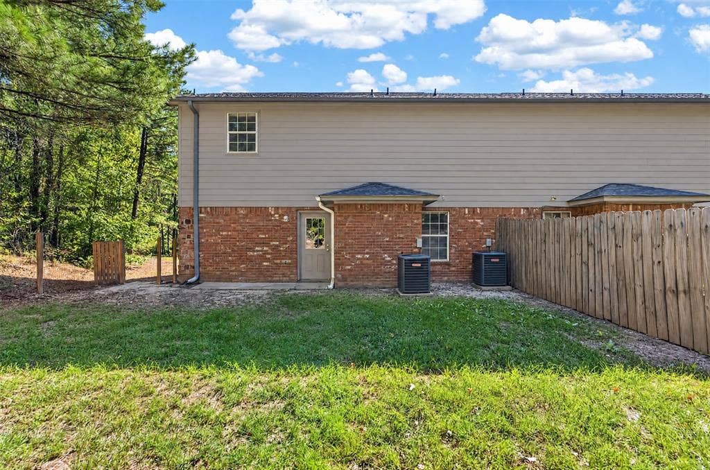 1708 Timber View Drive, Tyler, TX 75703 Rear exterior featuring horizontal lap siding, brick facade, wood-style privacy fencing, and two ground-level heating and cooling units