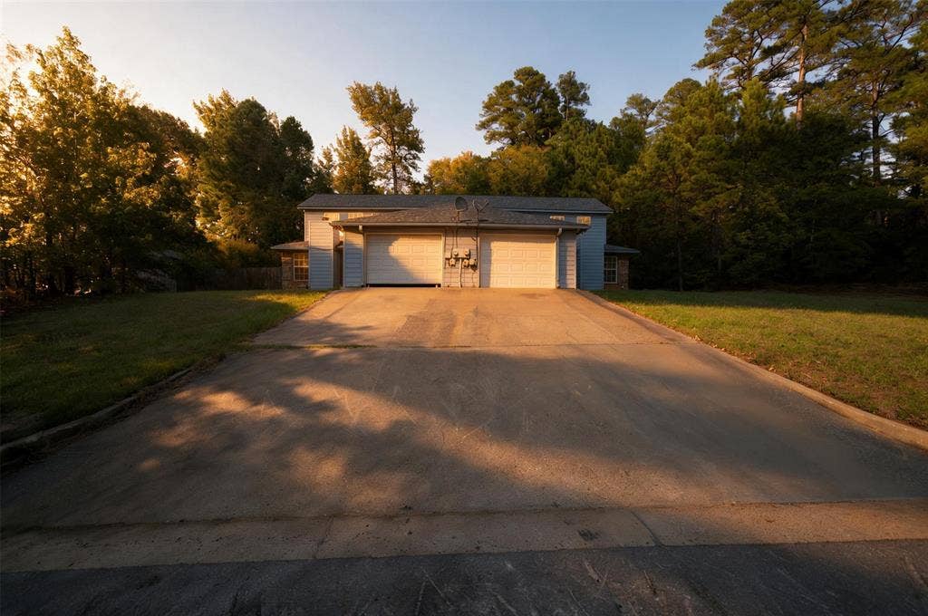 1708 Timber View Drive, Tyler, TX 75703 Exterior of a residence featuring a dual-bay garage, concrete driveway, and expansive lawn surrounded by mature trees