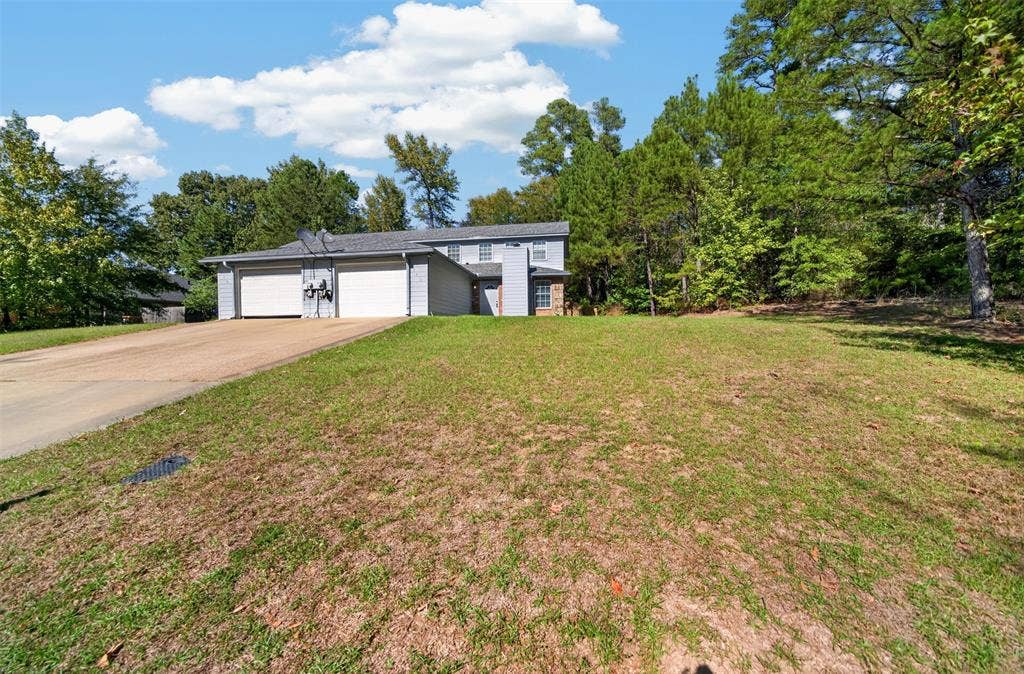 1708 Timber View Drive, Tyler, TX 75703 Multi-level exterior featuring horizontal siding, a two-car garage, an asphalt driveway, and a partially wooded lot