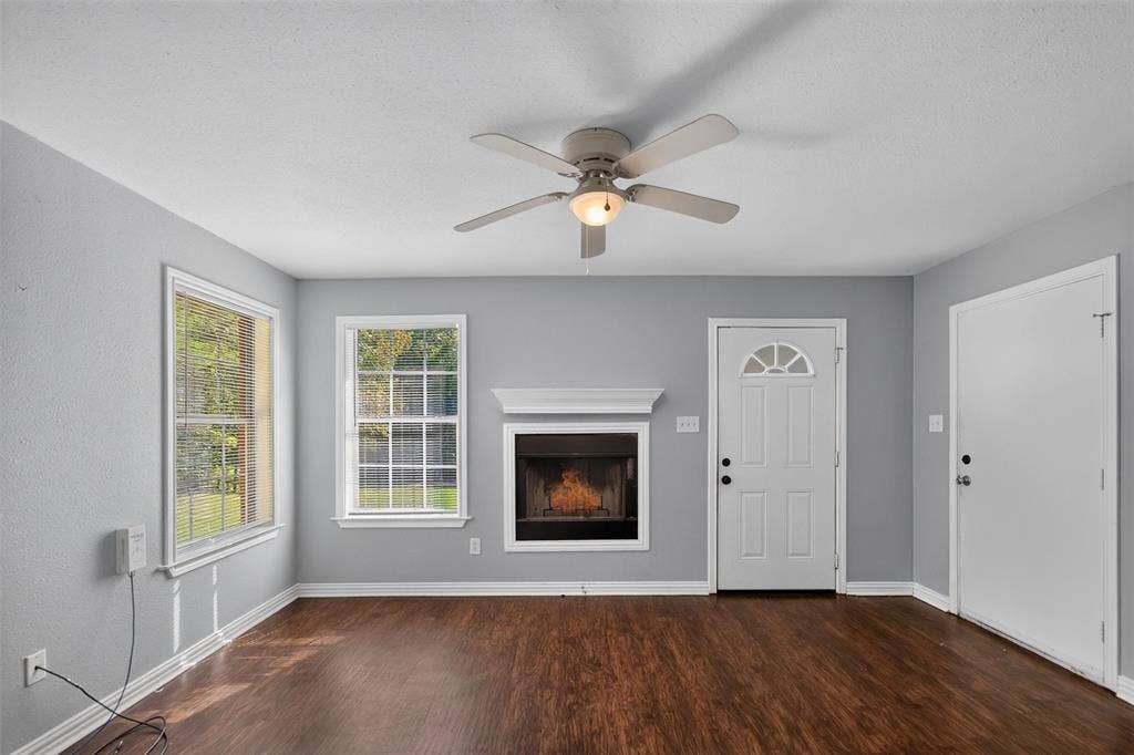 1708 Timber View Drive, Tyler, TX 75703 Living area featuring wood-finish flooring, a central fireplace with a decorative mantel, ceiling fan with integrated lighting, dual windows, and exterior door access