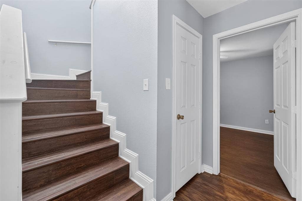 1708 Timber View Drive, Tyler, TX 75703 Staircase featuring wood-finish treads, white painted risers, and a wall-mounted handrail, accompanied by six-panel interior doors and wood-finish flooring