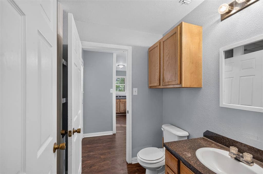 1708 Timber View Drive, Tyler, TX 75703 Wall-mounted natural wood cabinetry, dark-toned countertop with integrated sink, three-light vanity fixture, and white interior doors