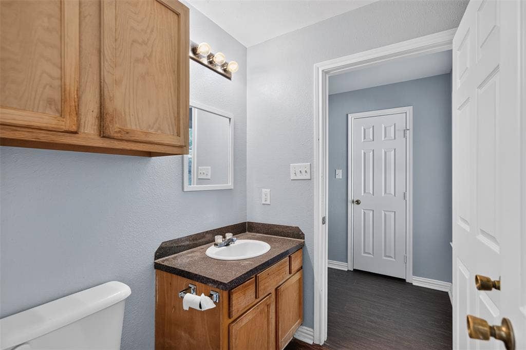 1708 Timber View Drive, Tyler, TX 75703 Built-in wood cabinetry, stone-finish vanity countertop with integrated sink, three-bulb vanity lighting, and wood-finish flooring