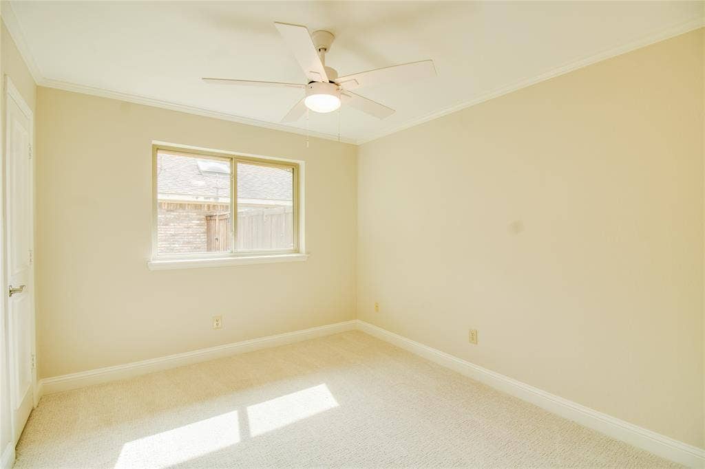 Neutral-toned room featuring wall-to-wall carpeting, a multi-blade ceiling fan with integrated lighting, a sliding window with a cream frame, and a solid-core interior door