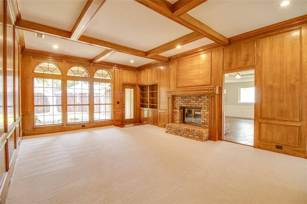 Wood-paneled walls with decorative molding, coffered ceiling, brick fireplace with a custom mantle, built-in shelving, and arched windows