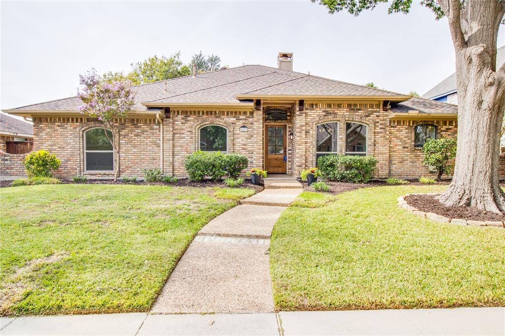 Brick exterior featuring arched window casings, a wood-framed front entry, hipped roofline, and aggregate concrete walkway
