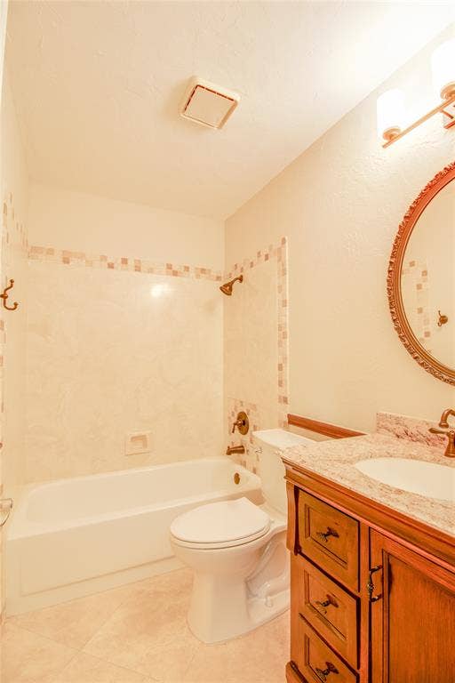 Bathroom featuring a wood vanity with stone-finish countertop, undermount sink, multi-tone tile tub surround, and metallic finish plumbing fixtures
