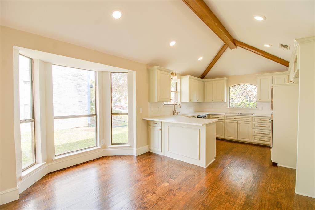 Kitchen featuring vaulted ceilings with exposed wood beams, wood-finish flooring, a bay window, recessed lighting, and a leaded glass accent window