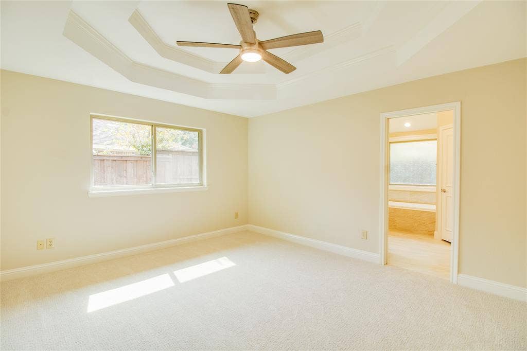Tray ceiling featuring a central five-blade ceiling fan with integrated lighting, neutral wall palette, and wall-to-wall carpeting