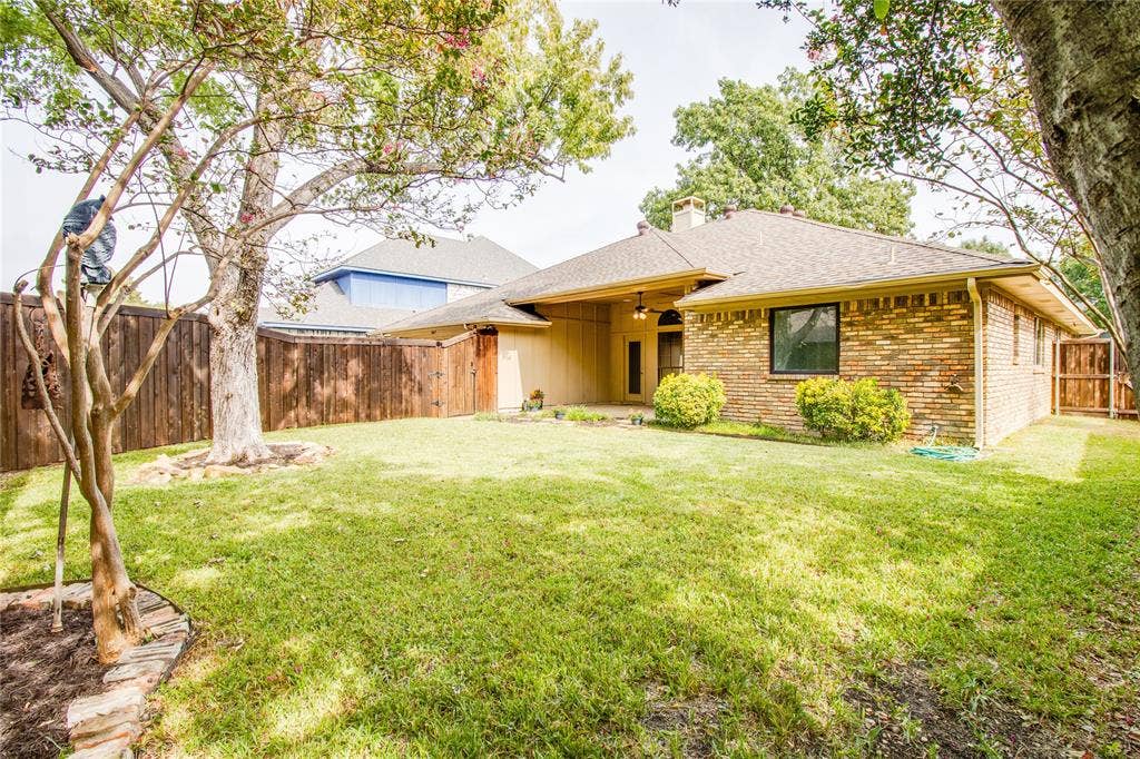 Backyard featuring a brick exterior, covered patio, wood privacy fencing, and established trees