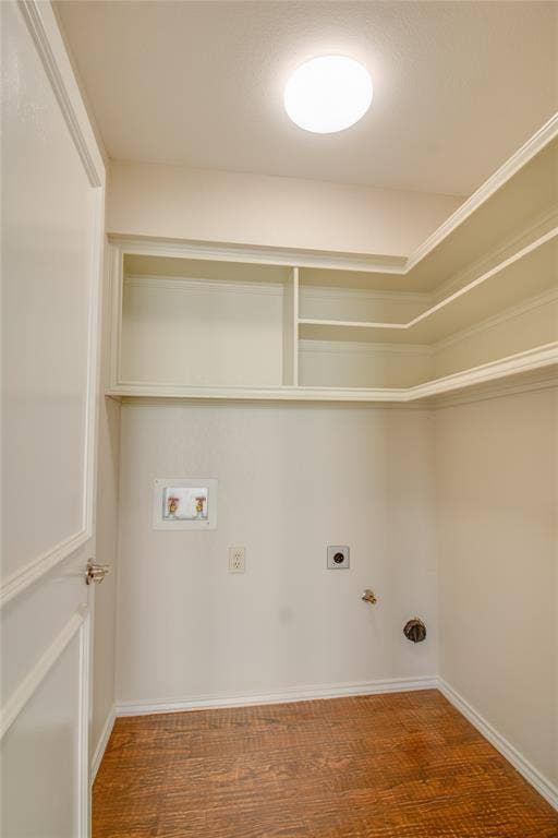 Utility space featuring wood-finish flooring, built-in tiered shelving, and dedicated water and electrical hookups
