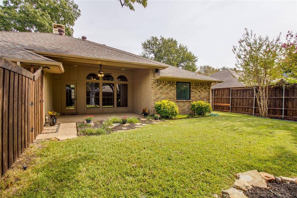 Covered concrete patio featuring an arched transom window, a ceiling fan, brick and horizontal siding exterior, and a fenced backyard with established landscaping