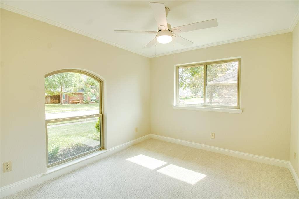 Neutral-toned room featuring a vaulted ceiling, arched window, sliding window, carpeted flooring, and a ceiling fan with integrated lighting