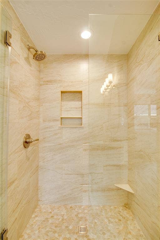 Walk-in shower featuring large-format stone-look tile walls, integrated recessed wall niche, pebble-stone flooring, frameless glass panel, and polished metal fixtures