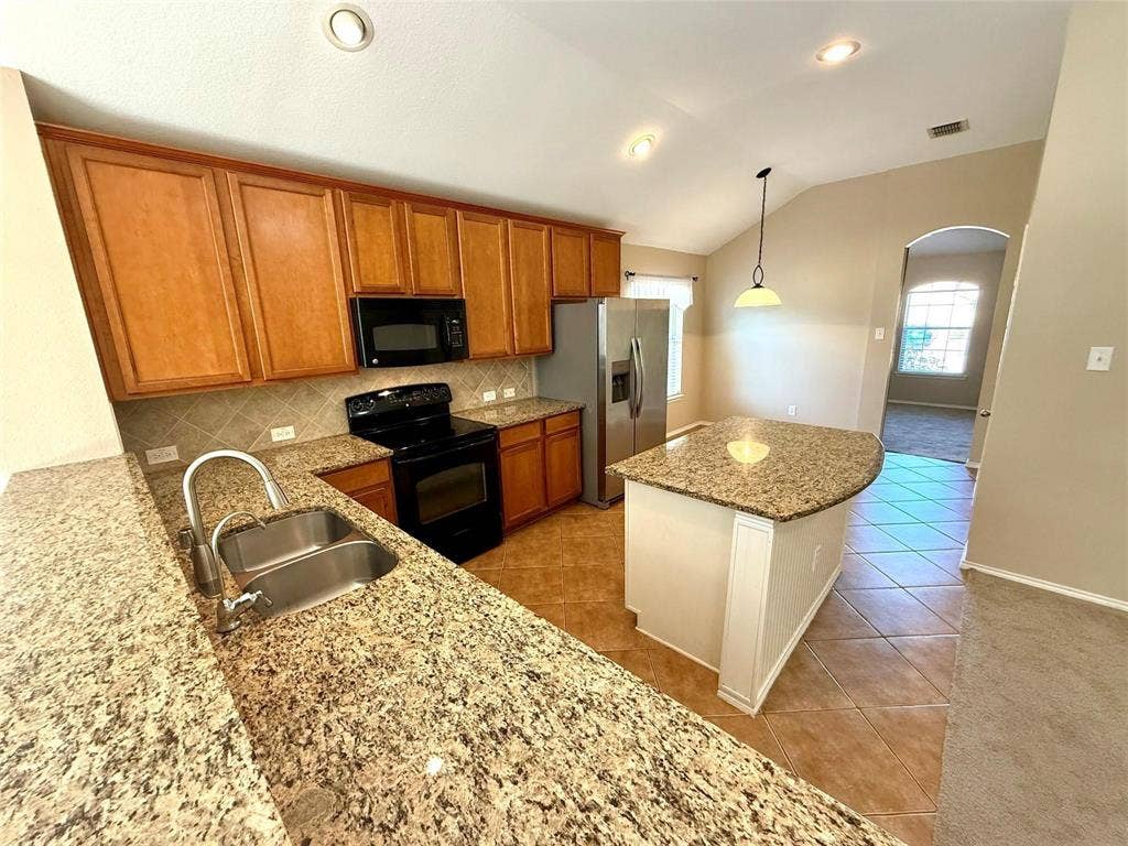 2111 Red River Road, Forney, TX 75126 Kitchen featuring natural stone countertops, custom wood cabinetry, stainless steel appliances, a center island, and tile flooring under a vaulted ceiling