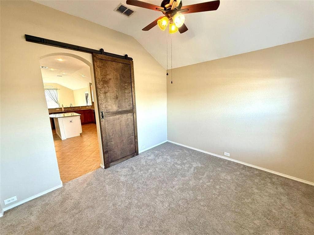 2111 Red River Road, Forney, TX 75126 Vaulted ceiling featuring a central ceiling fan with integrated lighting, a sliding wood-finish door with black hardware, and neutral wall-to-wall carpeting