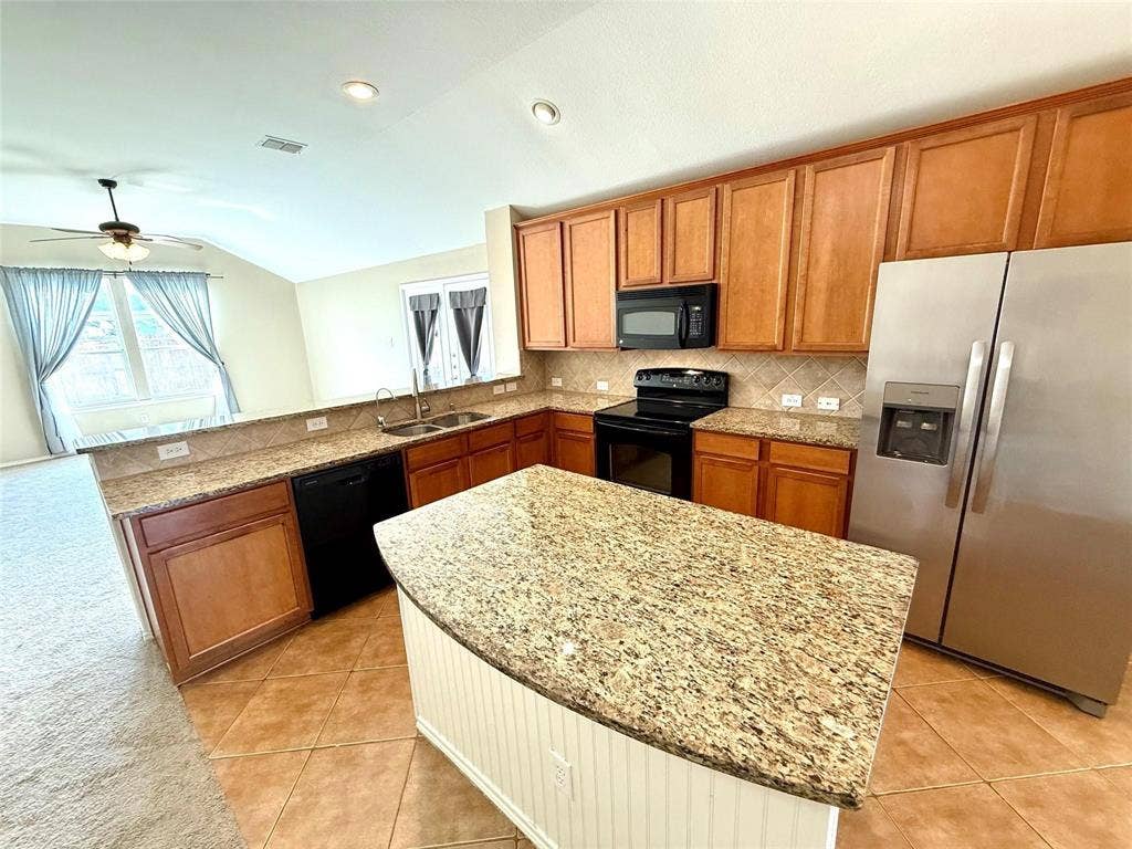 2111 Red River Road, Forney, TX 75126 Kitchen featuring a center island, stone-patterned countertops, stainless steel appliances, stained cabinetry, and tile flooring