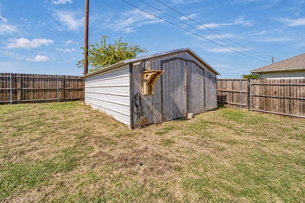 413 Bonnie Court, Anna, TX 75409 Exterior storage shed featuring corrugated metal siding, double swinging doors, and a wood-slatted exterior wall, situated within a fenced backyard