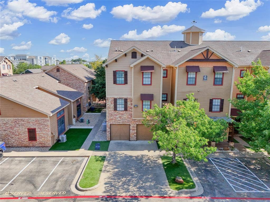 2410 S 2nd Street, #625, Waco, TX 76706 Multi-story exterior featuring a mix of horizontal lap siding and masonry stone veneer, dual attached garages, a shingled roof with a decorative cupola, and defined parking areas