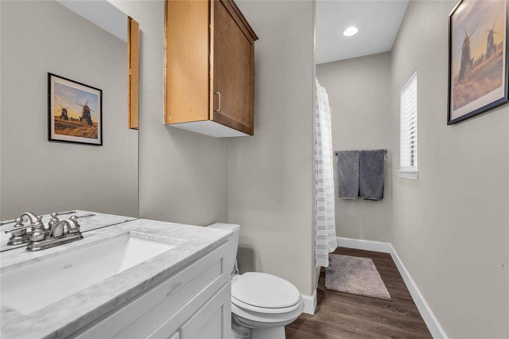 2410 S 2nd Street, #625, Waco, TX 76706 Bathroom featuring a white vanity cabinet with stone-finish countertop, undermount sink, dual-handle faucet, wood-finish flooring, and wall-mounted cabinetry