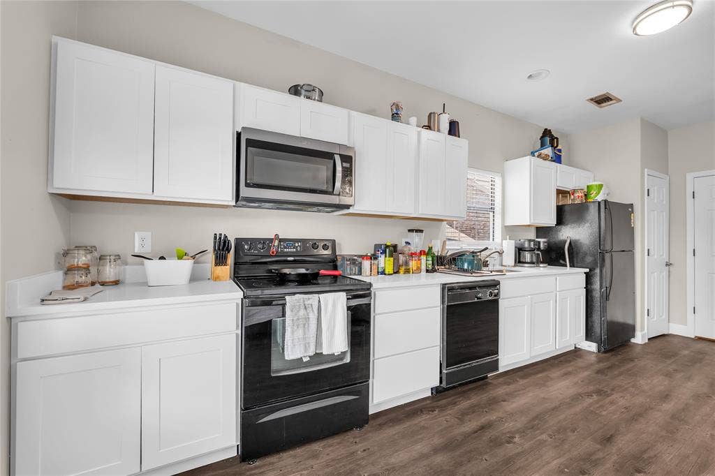 2410 S 2nd Street, #625, Waco, TX 76706 Kitchen featuring white cabinetry, solid surface countertops, wood-finish flooring, and a suite of black appliances including a built-in microwave and range