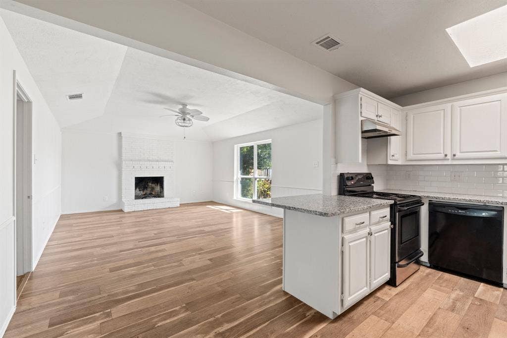 8406 Lullwater Drive, Dallas, TX 75218 Open-concept interior featuring wood-finish flooring, a white painted brick fireplace, shaker-style cabinetry, stone countertops, and a subway tile backsplash