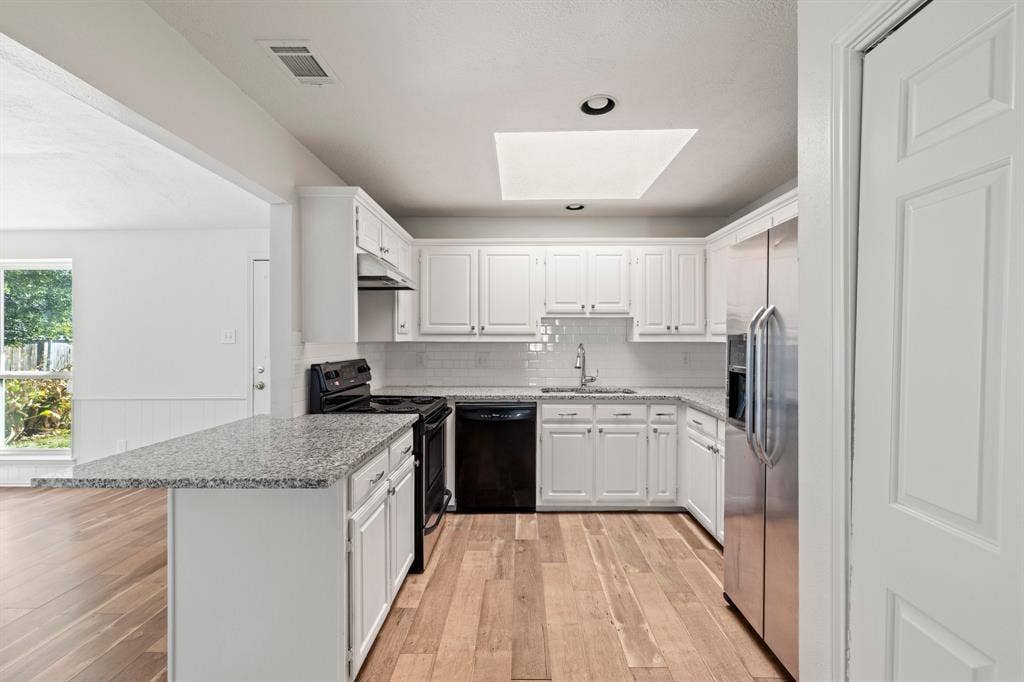 8406 Lullwater Drive, Dallas, TX 75218 Kitchen featuring white cabinetry, stone-finish countertops, subway tile backsplash, wood-finish flooring, and a ceiling skylight