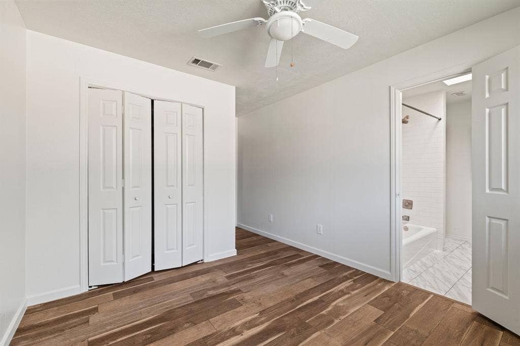 8406 Lullwater Drive, Dallas, TX 75218 Interior room featuring wood-finish flooring, white paneled bi-fold closet doors, and a ceiling-mounted fan with integrated light