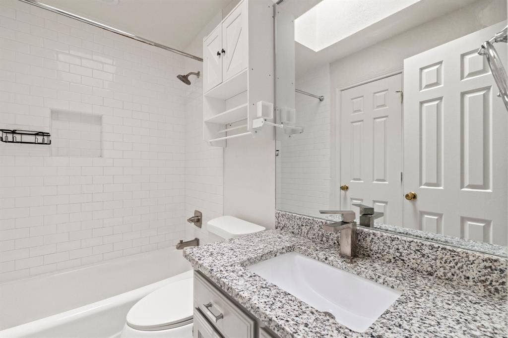 8406 Lullwater Drive, Dallas, TX 75218 Bathroom featuring subway tile shower surround with integrated recessed niche, stone-finish countertop with undermount sink, built-in cabinetry, and wall-mounted vanity mirror