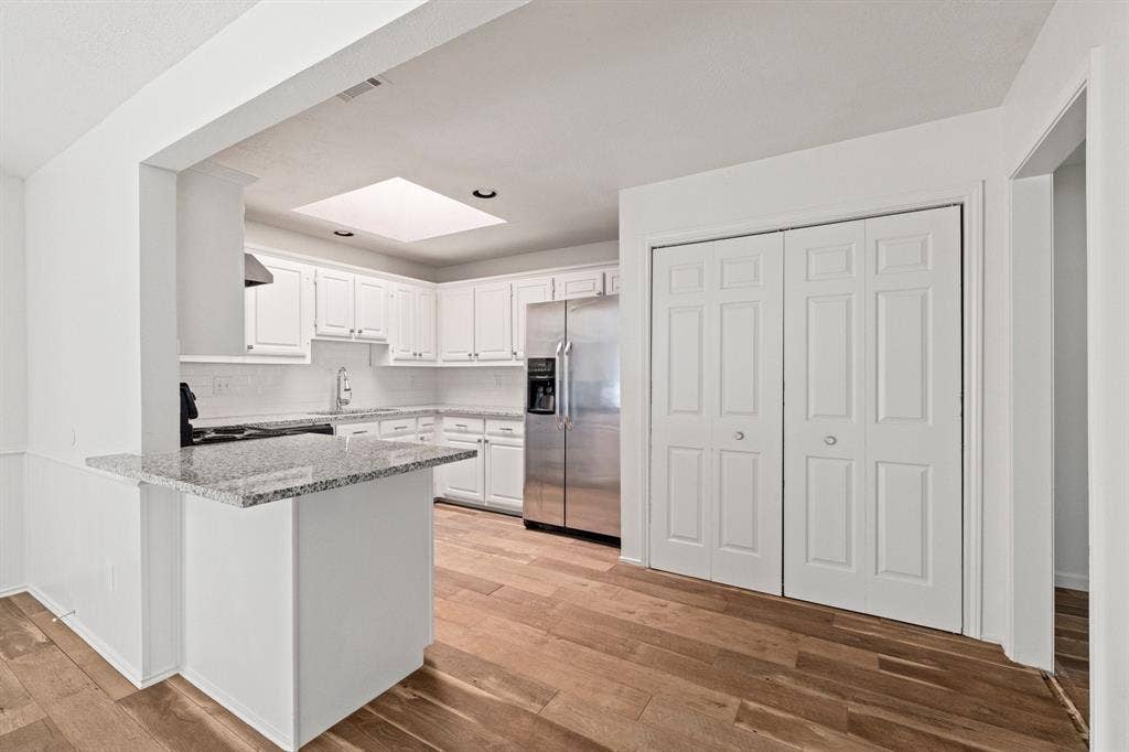 8406 Lullwater Drive, Dallas, TX 75218 Kitchen featuring white cabinetry, stone countertops, stainless steel refrigerator, skylight, and wood-finish flooring