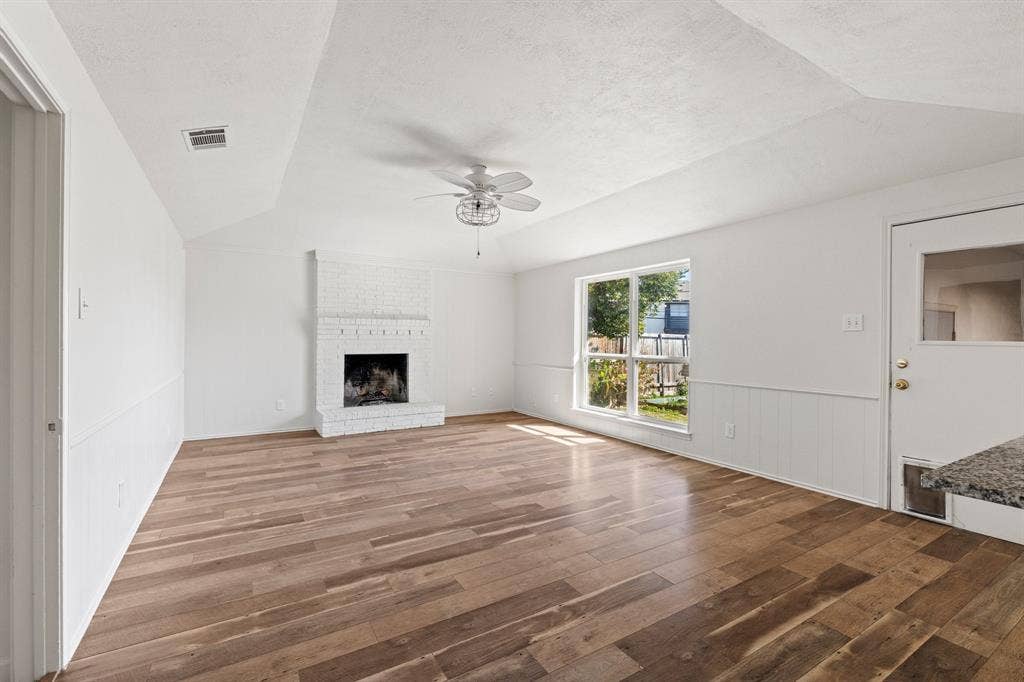 8406 Lullwater Drive, Dallas, TX 75218 Vaulted ceilings, wood-finish flooring, white painted brick fireplace, large picture window, and wainscoting