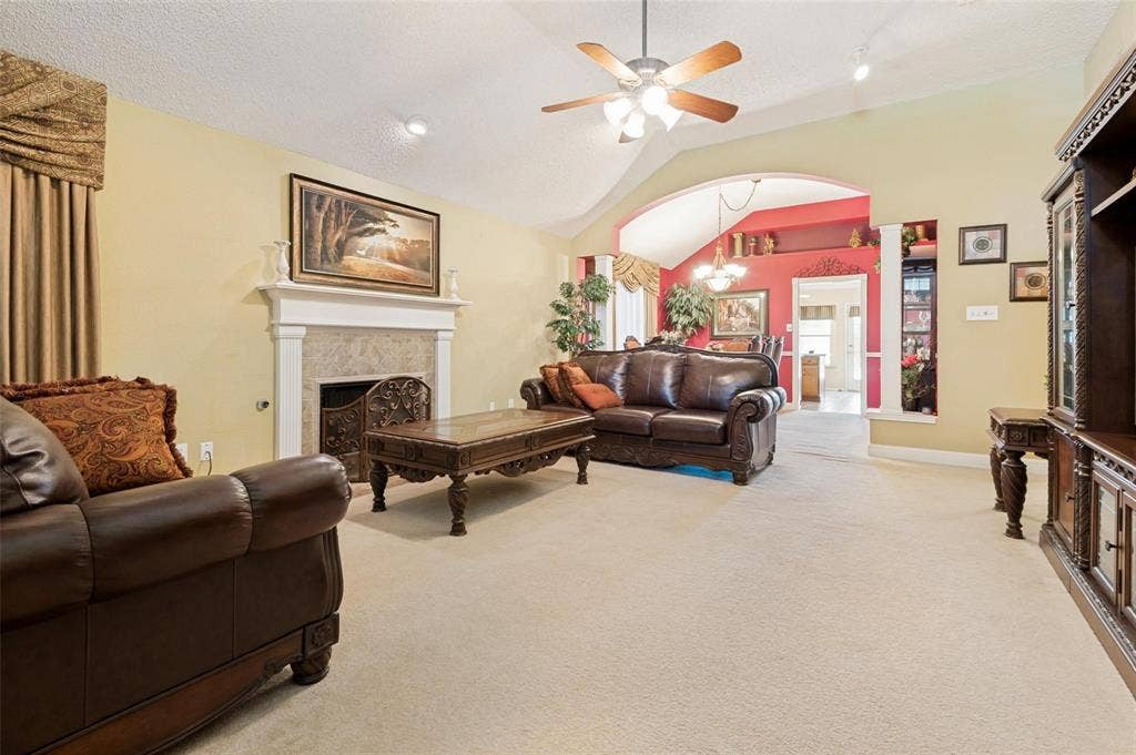 Vaulted ceilings, fireplace with a decorative mantel, arched architectural detail, and neutral carpeting