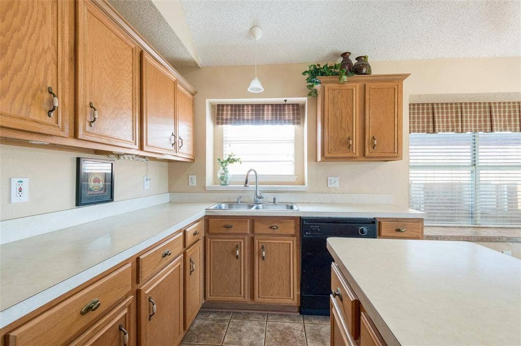 Kitchen featuring natural wood cabinetry, solid-surface countertops, a stainless steel dual-basin undermount sink with a gooseneck faucet, tile flooring, and a pendant light fixture