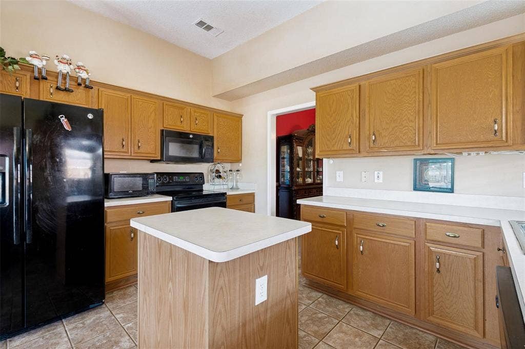 Kitchen featuring natural-finish wood cabinetry, a central island, solid-surface countertops, and tiled flooring