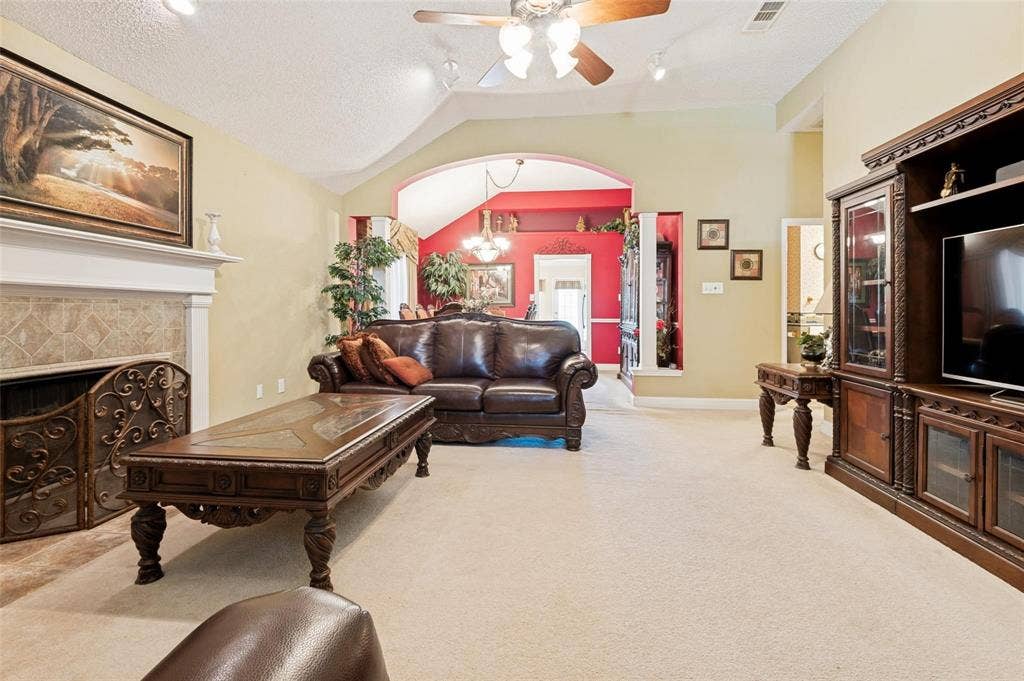 Living area featuring a vaulted ceiling, fireplace with tile surround, decorative mantel, archway with architectural columns, and ceiling fan