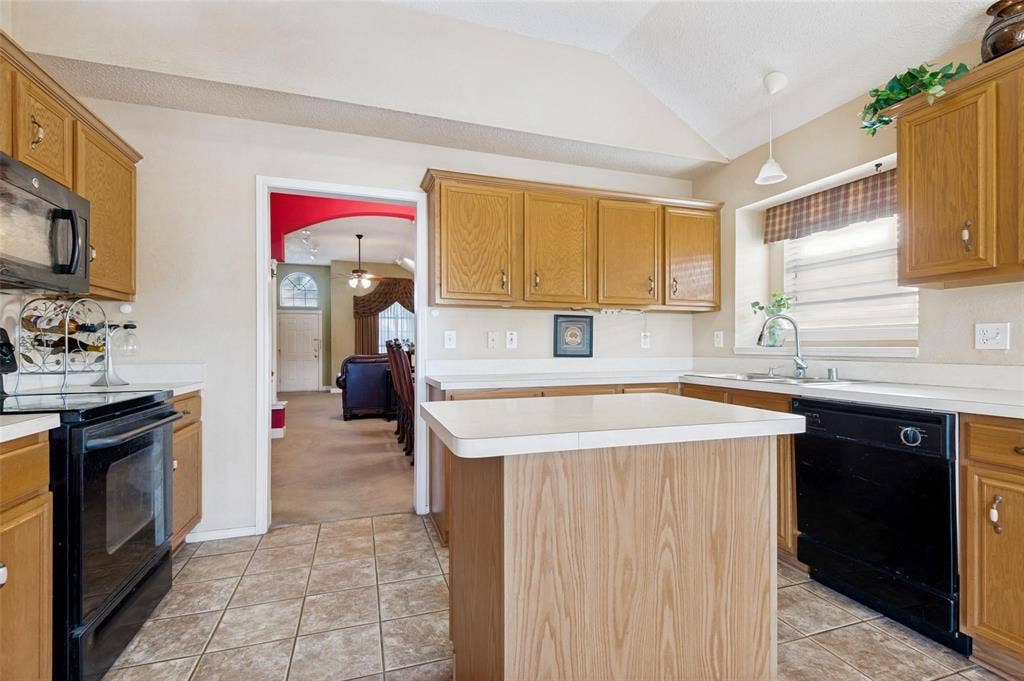 Kitchen featuring oak-finish cabinetry, central island with solid-surface countertop, tiled flooring, and vaulted ceiling