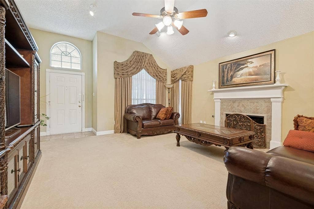 Vaulted ceiling with a ceiling fan, arched window, and stone-surround fireplace with a classic mantel