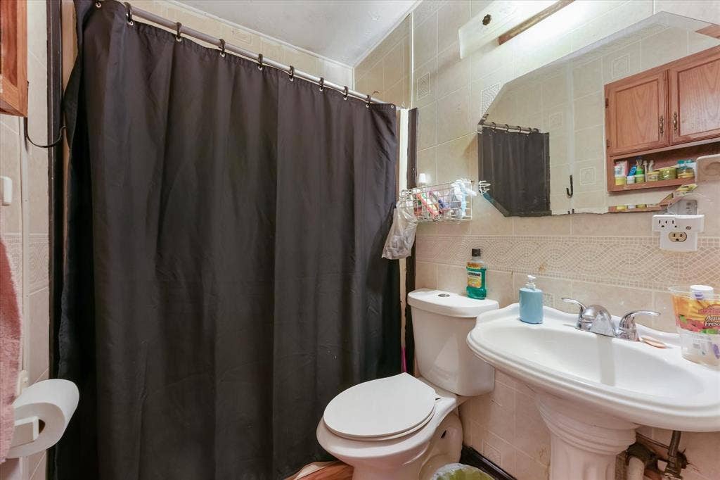 201 Glenridge Drive, Mesquite, TX 75149 Bathroom featuring wall-to-wall ceramic tiling, a pedestal sink with dual-handle chrome faucet, a wall-mounted medicine cabinet with wood-finish cabinetry, and a large beveled-edge mirror