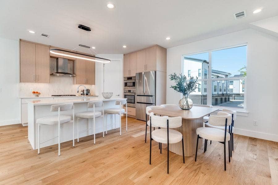 Kitchen featuring light wood-finish cabinetry, quartz countertops, a waterfall-edge island, stainless steel built-in appliances, and wood-finish flooring