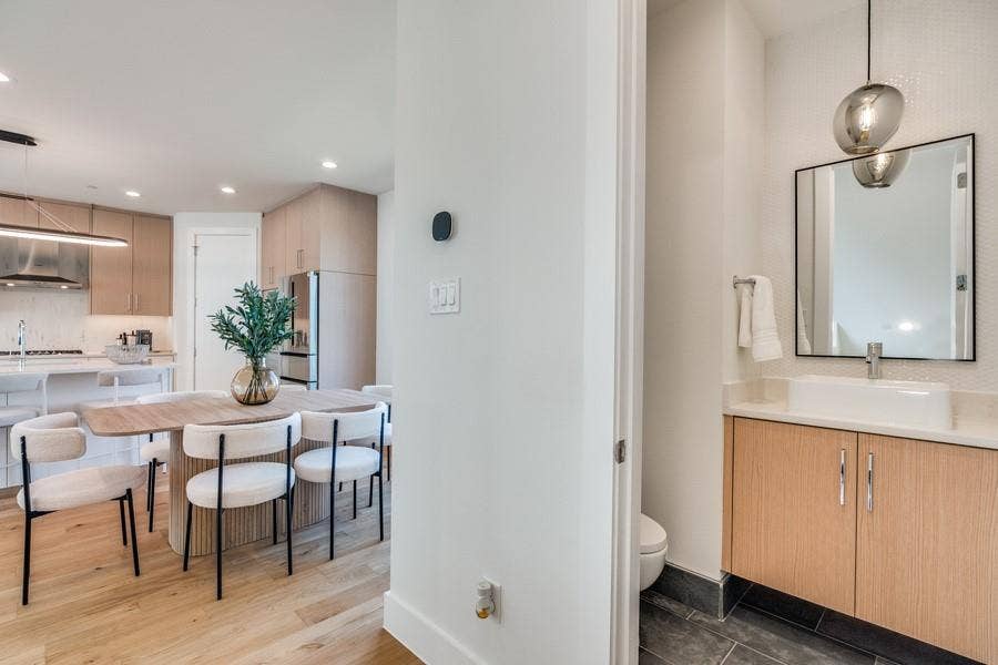Bathroom featuring a floating wood-finish vanity, rectangular vessel sink, geometric mirror, and pendant lighting, complemented by wood-finish flooring and stone-finish floor tile